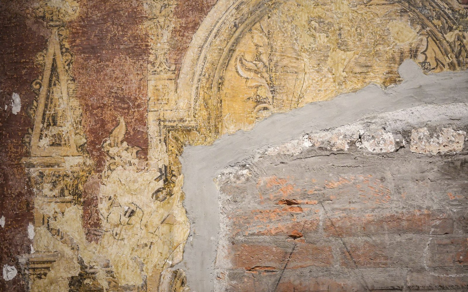 Faded fresco fragments on a wall alongside exposed brick and fresh plaster