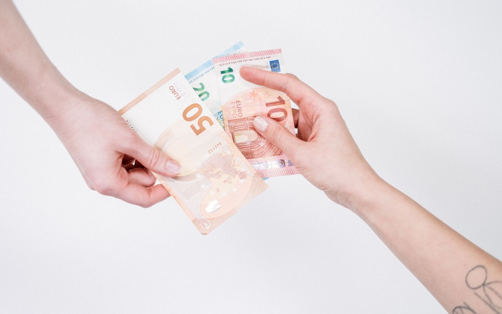 Two hands exchanging euro banknotes of various denominations against a white background