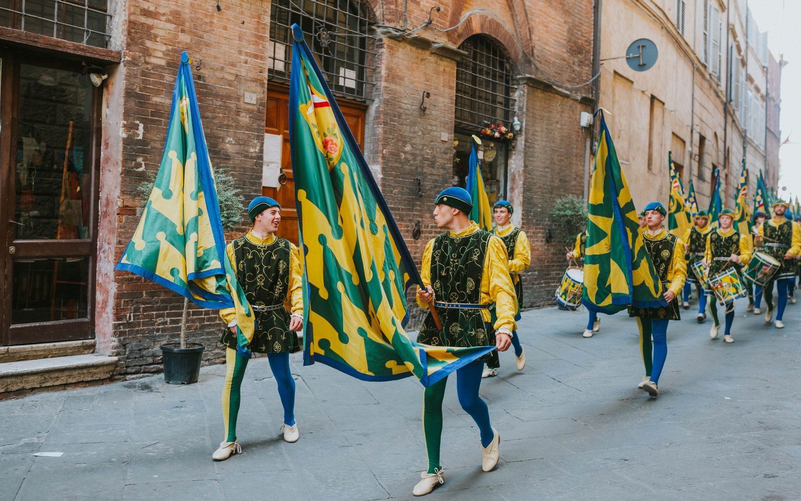 Costumed flag bearers in medieval dress parade down a narrow cobblestone street